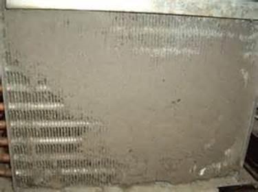 Refrigerator grate over coils nearly completely covered by dirt and debris.