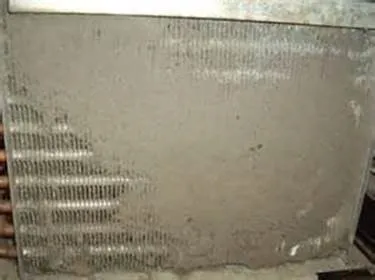 Refrigerator grate over coils nearly completely covered by dirt and debris.